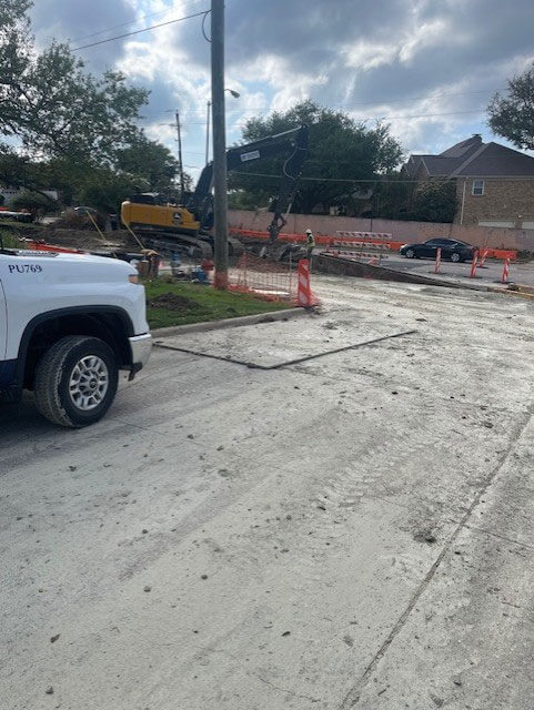 Orange-and-white barricades closing the road with construction equipment present, indicating no vehicle access.